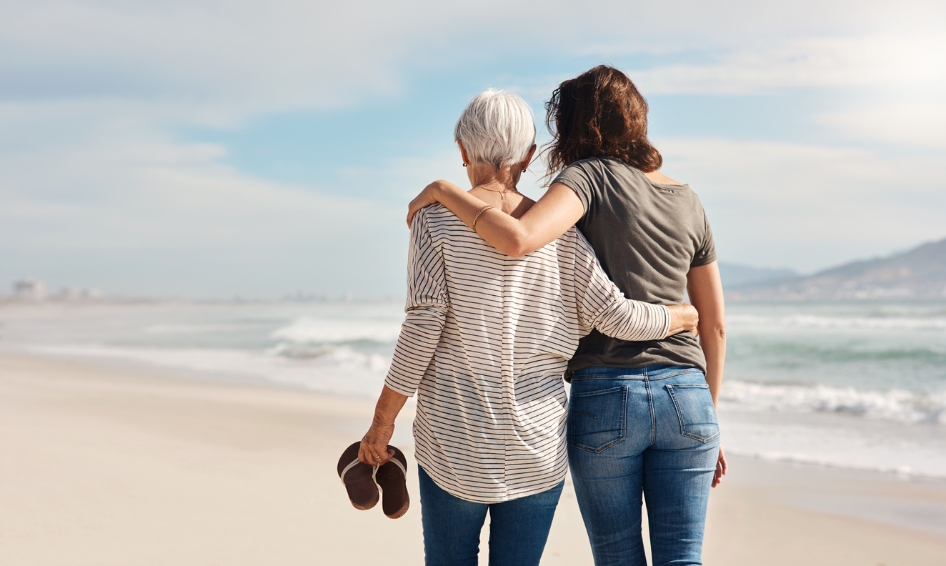 pre paid funeral plan - A woman going for a walk along the beach with her elderly mother