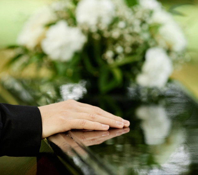 Funeral Directors Wirral Services. An image of a hand on a black coffin saying goodbye at an outdoor funeral ceremony.